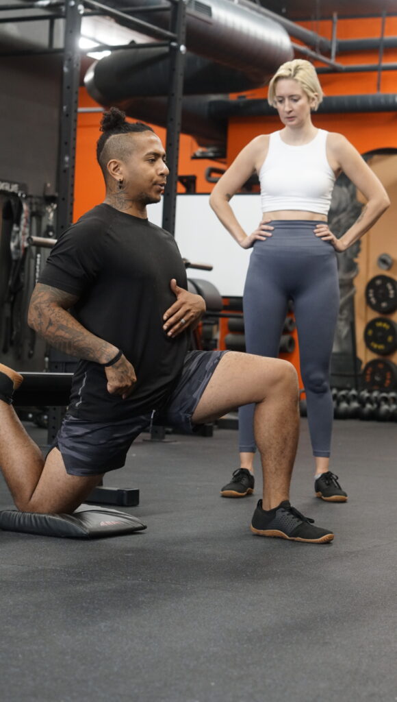 Coach Moose demonstrating a stretching technique to a client at AMPT Fit gym, focusing on proper form and body alignment. The session reflects AMPT Fit's holistic approach to personalized training, which combines physical fitness with mindfulness and mental well-being.