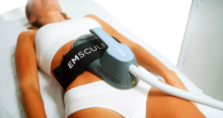 Client undergoing an Emsculpt NEO session at AMPT Fit, lying comfortably on a treatment bed with the device applied to their abdominal area. The procedure is monitored in a professional setting, showcasing the use of non-invasive technology for body contouring.